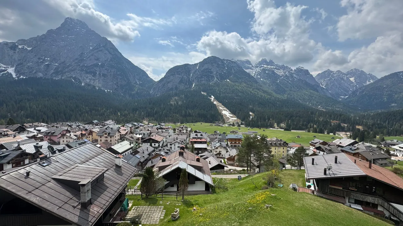 The view from the balcony, under that day's sky: the roofs of Sappada, the ski run through the woods and the peaks opposite