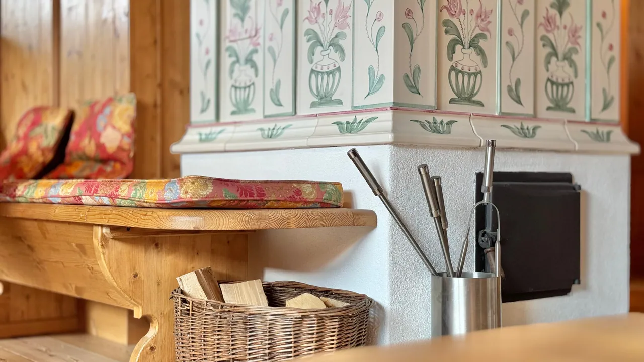 Detail des mit Blumen bemalten Kachelofens mit der Holzbank daneben